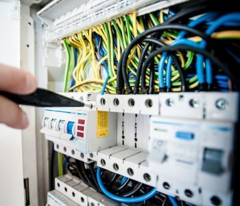 Hand of electrician working on a circuit breaker panel with colorful wires, ensuring safe electrical connections.